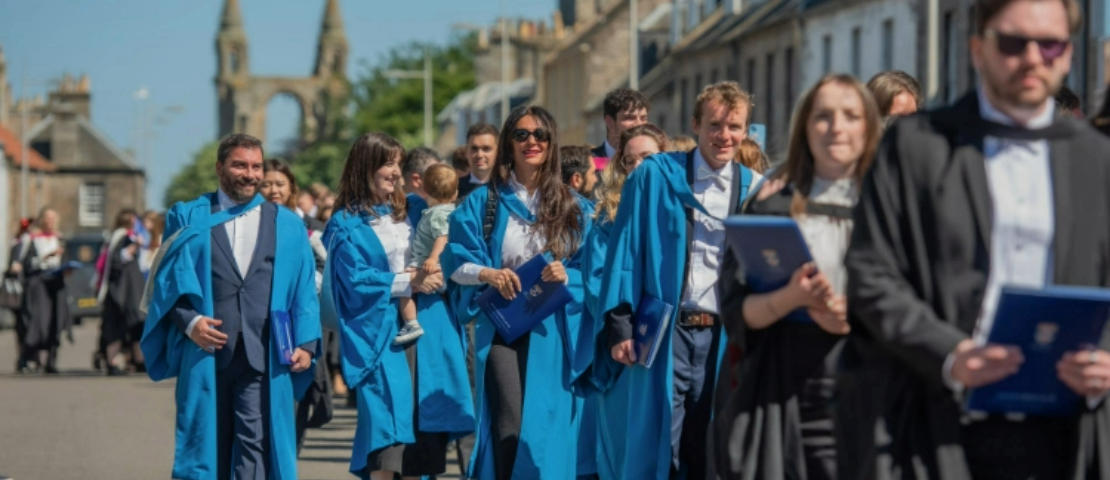St Andrews PhD graduates, dressed in blue gowns, process down North Street in the sun